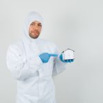 Male doctor in protective suit, gloves pointing at house model and looking gentle , front view.